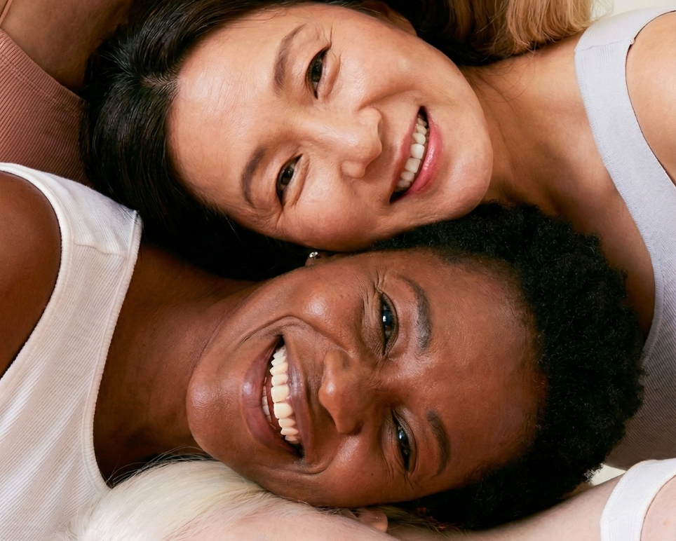 Four women of different ethnicities lying on a white background, smiling.